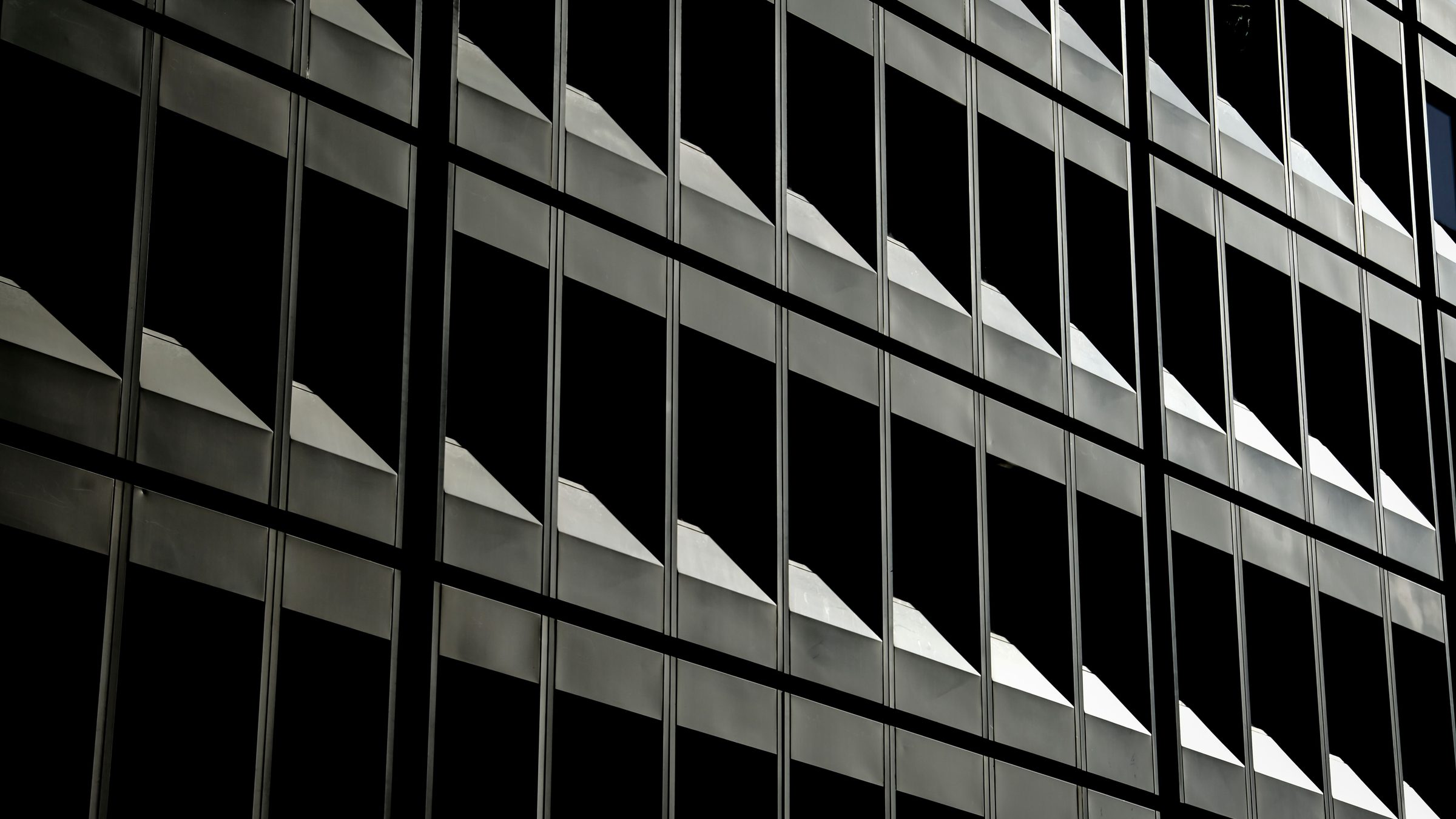 Repeating window bays across a dark glass office facade, each catching a wedge of light.